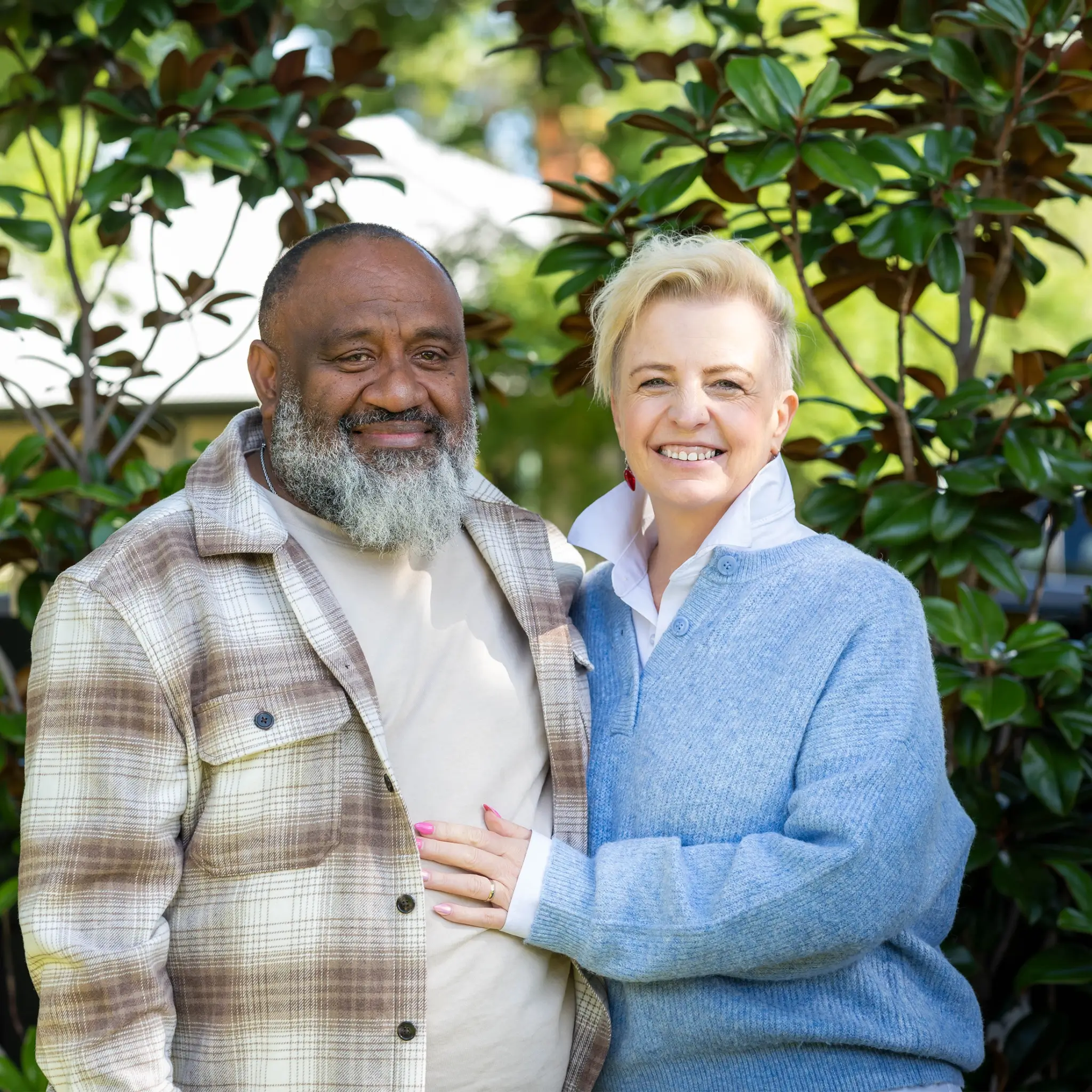 MyBudget clients, Kim & Bob. They are a smiling middle-aged couple standing close outside. Bob has a grey beard and flannel shirt; Kim has short blonde hair.
